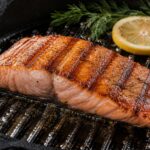 grilovany-losos-panev Grilovaný filet z lososa s patrnými otisky grilu na černé litinové grilovací pánvi, doplněný plátkem citronu a snítkou kopru.